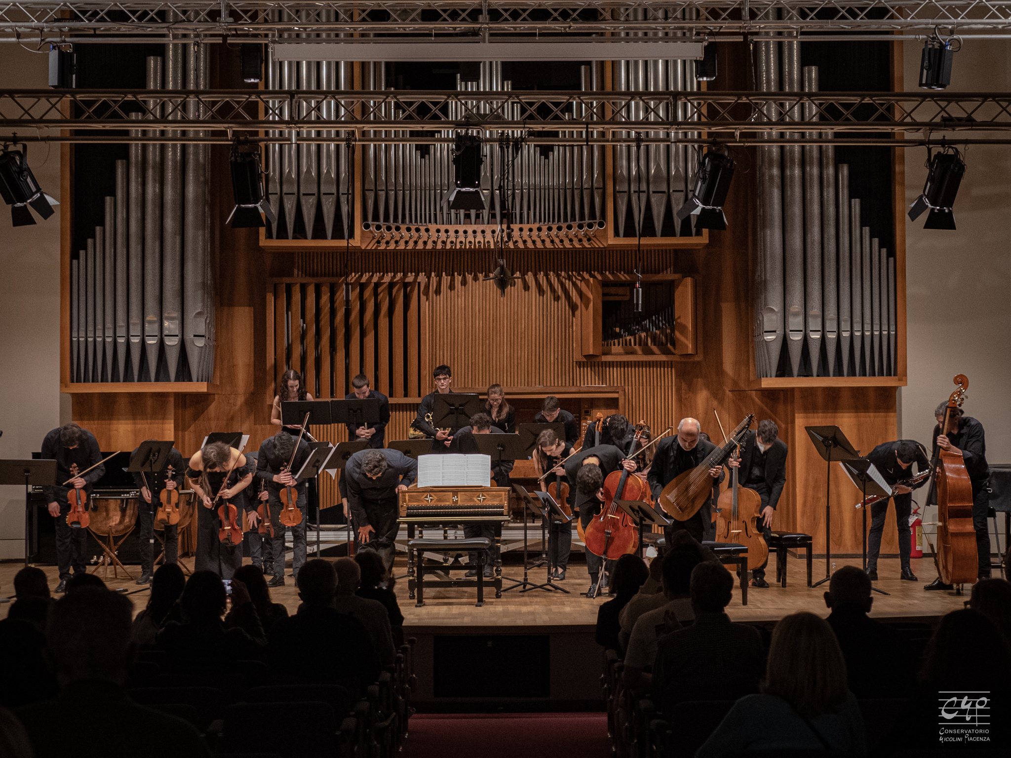 Un ensemble barocco si inchina a fine concerto sul palco del Salone del Nicolini, sotto l’organo e l’americana con le luci.