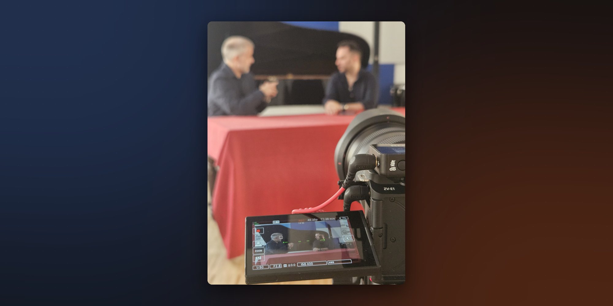 Il set di un Nicolini Talk, luglio 2025: in primo piano lo schermo della camera che registra in 4K, dietro i due ospiti seduti al tavolo con la tovaglia rossa.