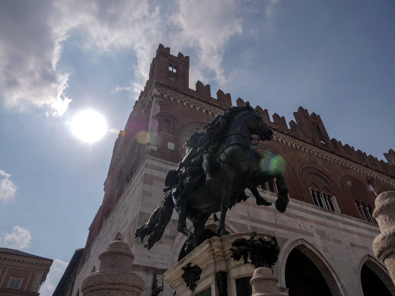 Piazza Cavalli against the light: the Palazzo Gotico, the equestrian statue and the sun among the clouds, a frame from the timelapse