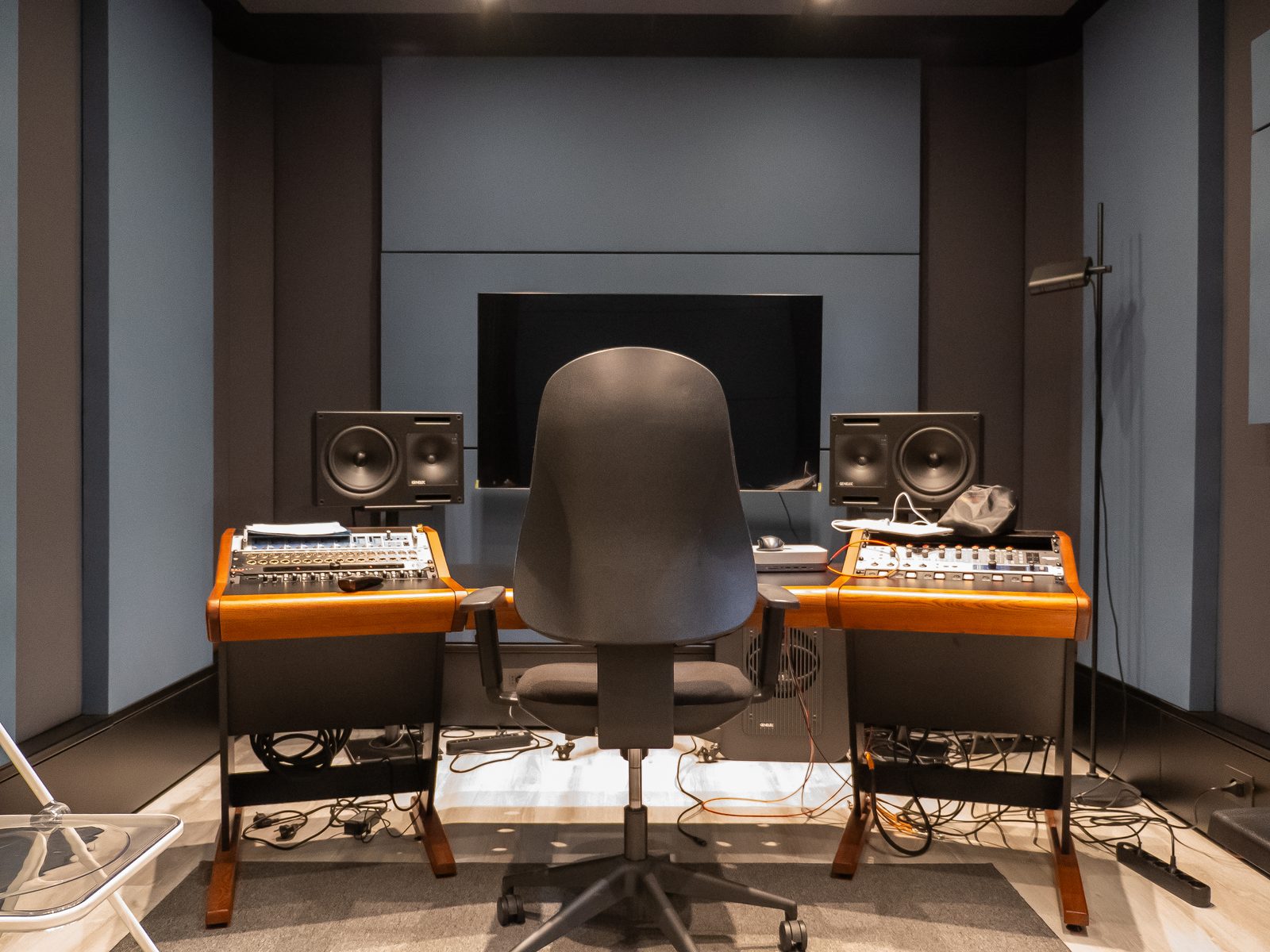 La regia di XNL Musica, vuota: la scrivania in legno con due mixer, i monitor da studio ai lati dello schermo e la sedia al centro.