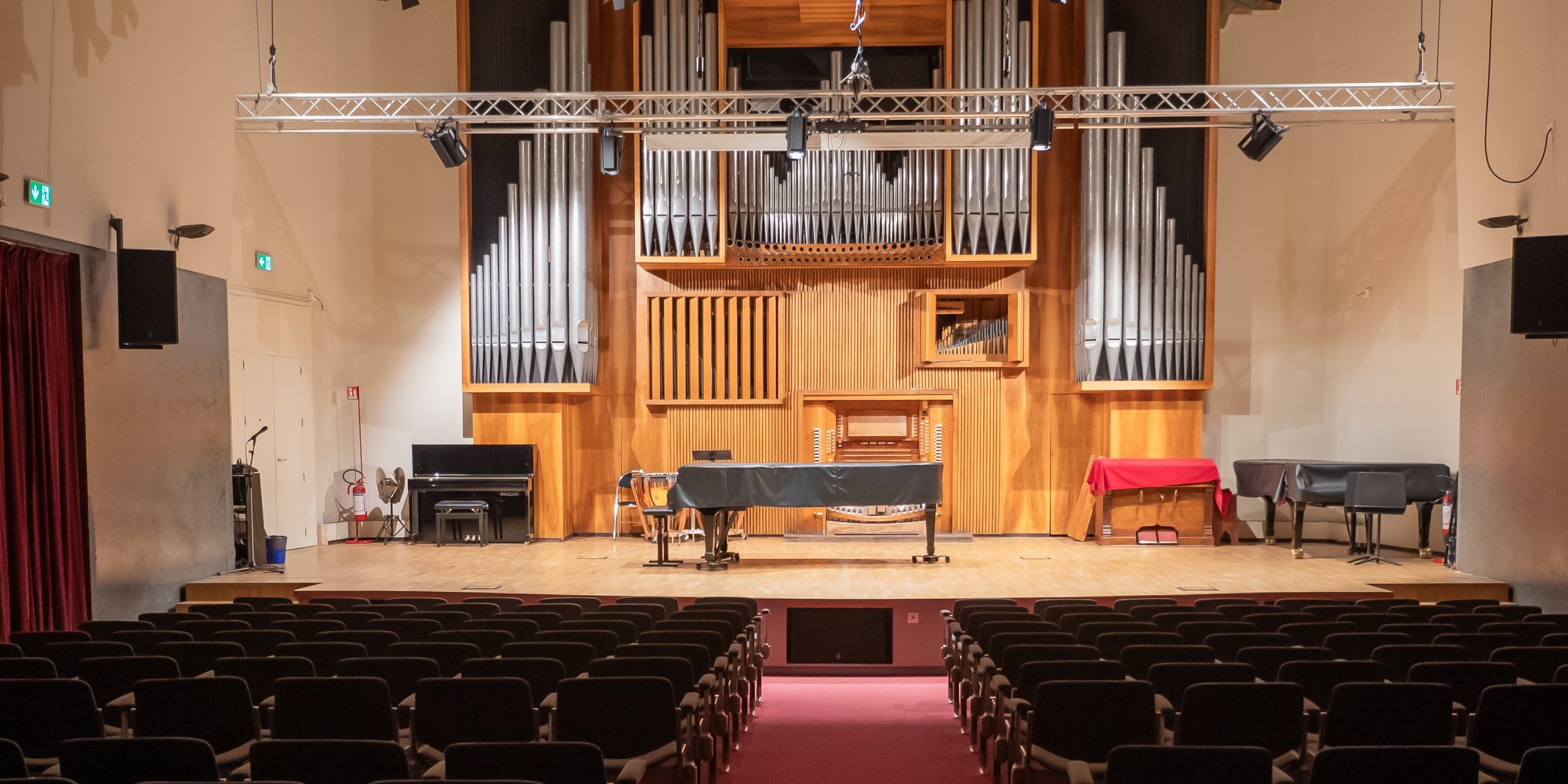 Il Salone del Nicolini vuoto, visto dalla platea: l’organo, il palco con i pianoforti, l’americana con i fari e i microfoni appesi, i diffusori alle pareti.