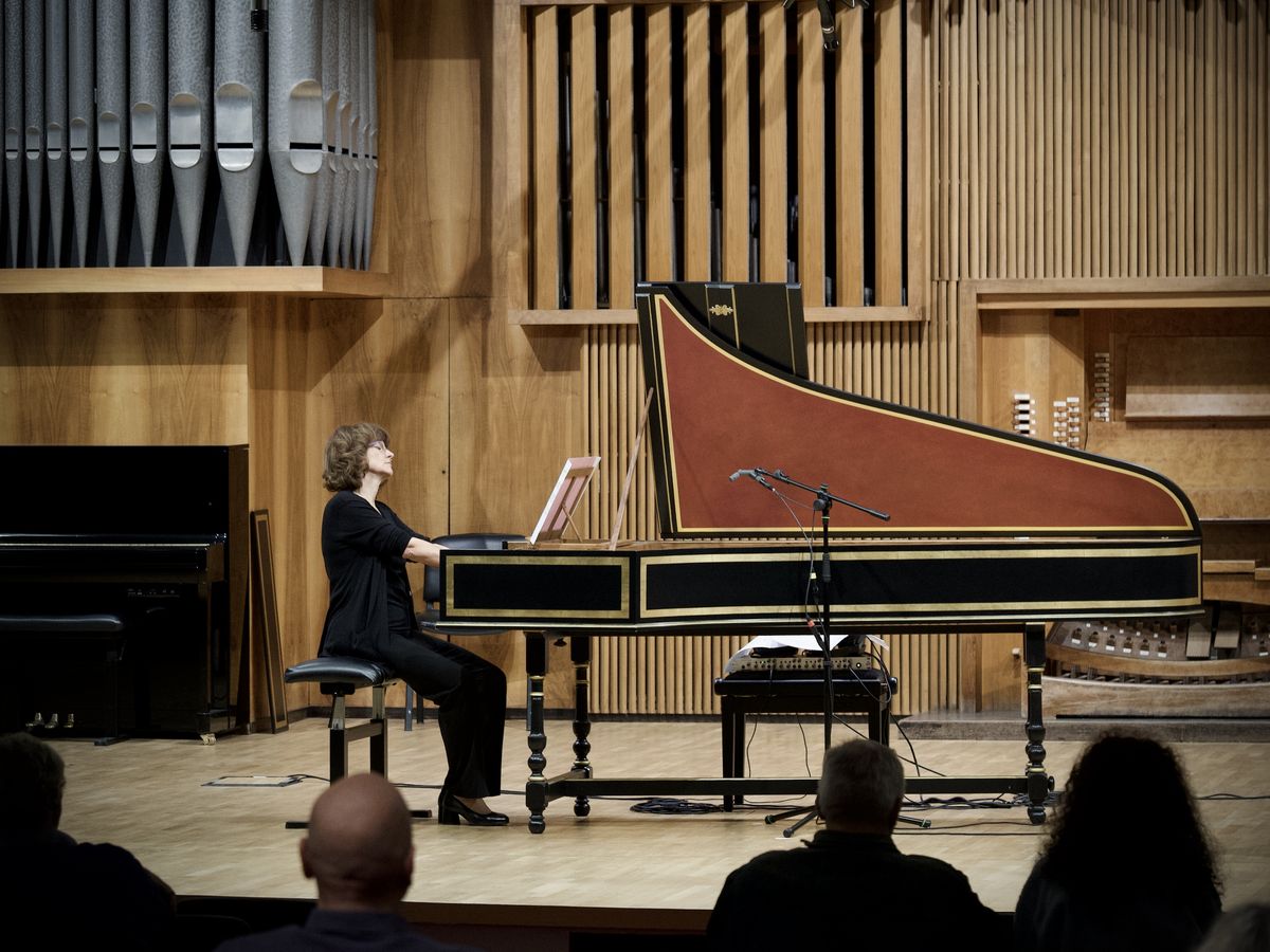 A harpsichordist on stage, with the organ pipes behind her and the audience in the foreground.