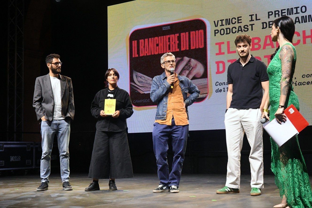 The IlPod stage in Piazza Cavalli on the evening of 23 September: four people standing in front of the screen showing the cover of the winning podcast, and the host with the microphone.