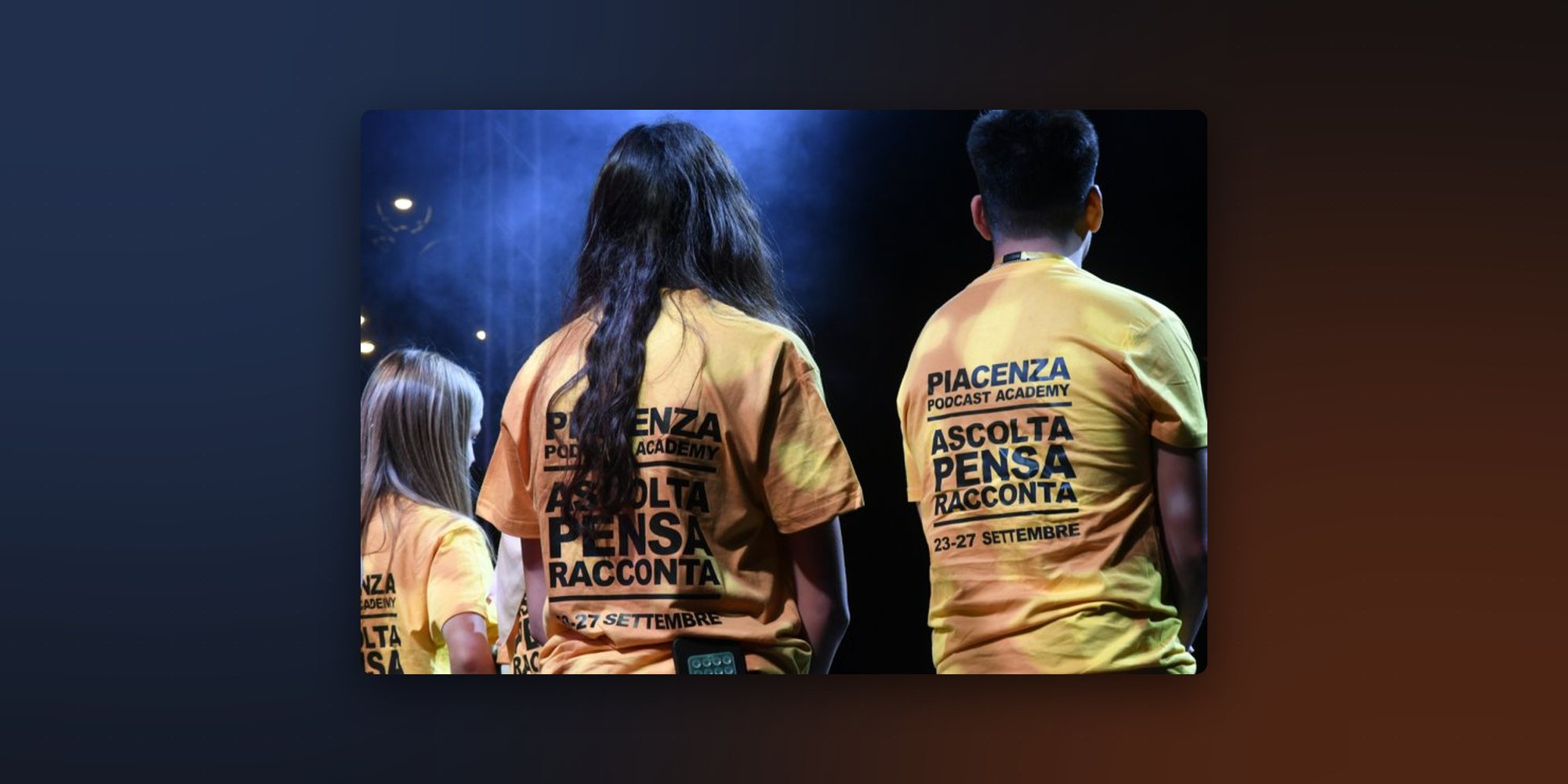 Ragazze e ragazzi della Piacenza Podcast Academy di spalle sul palco, con le magliette gialle «Ascolta Pensa Racconta».