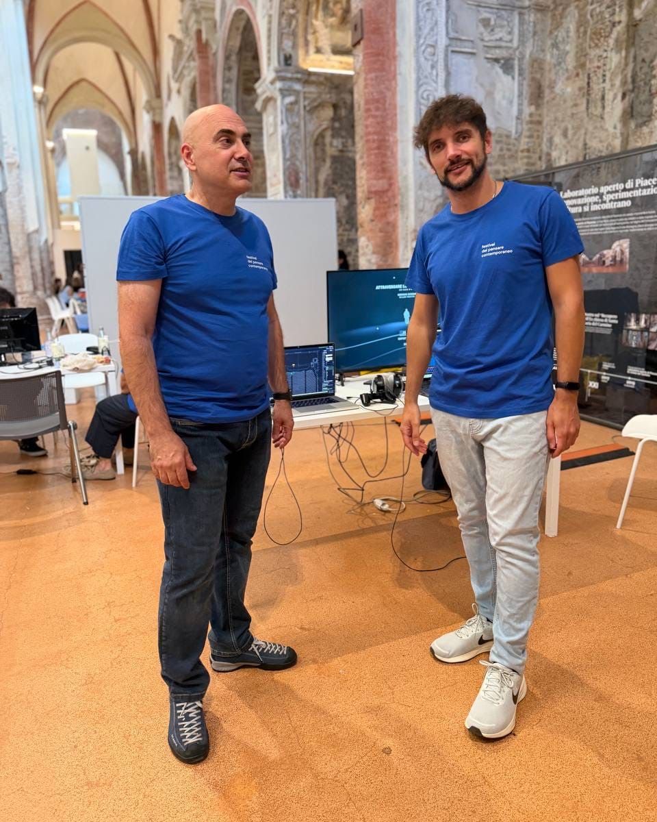Due persone con la maglietta blu del festival in piedi nella navata del Carmine; dietro di loro la postazione e uno schermo con la scritta «Attraversare il suono».