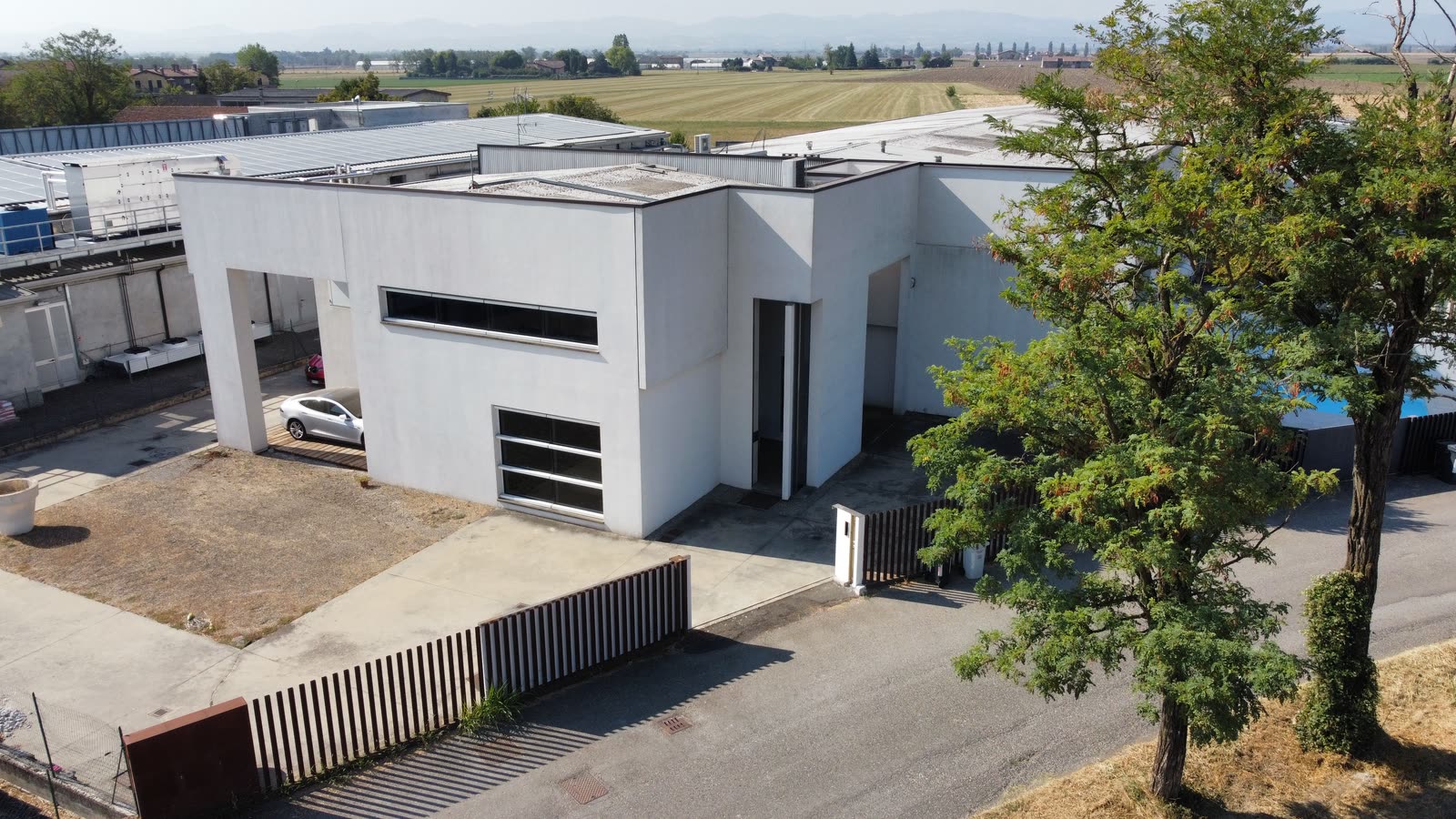 Lo studio visto dal drone: un edificio bianco a volumi squadrati, con il portico, il cancello e la campagna piacentina sullo sfondo
