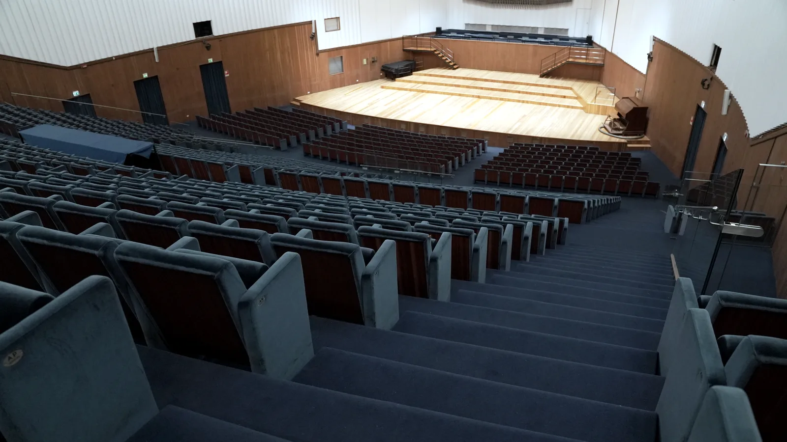 The empty Sala Verdi seen from the back rows: grey-blue seats sloping down to the pale wooden stage, the slatted walls, the white above and, at the back, the organ pipes.