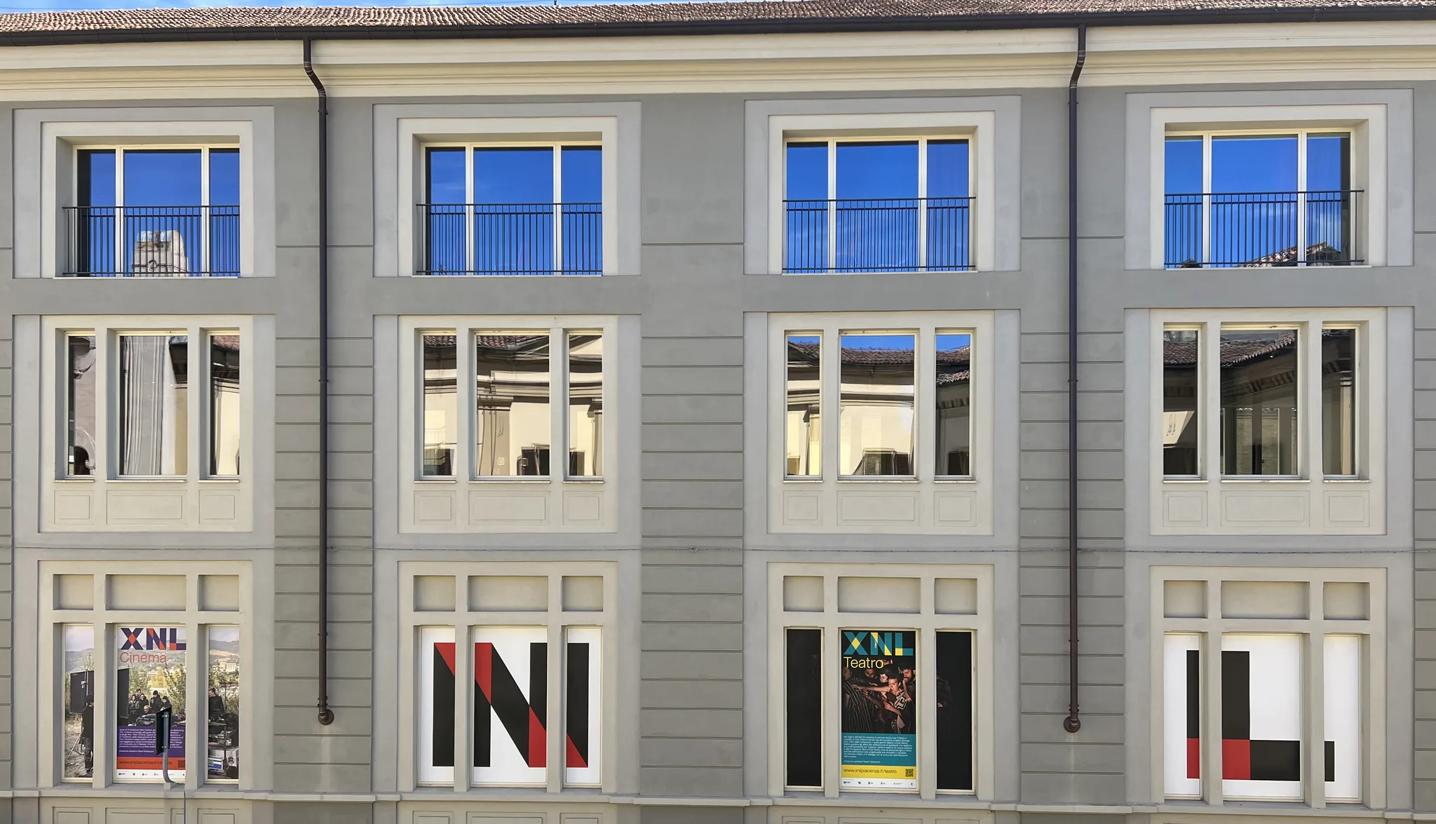 La facciata di XNL in via Santa Franca, di giorno: tre piani, dodici finestre; in quelle del piano terra i manifesti di XNL Cinema e Teatro e le lettere N e L.